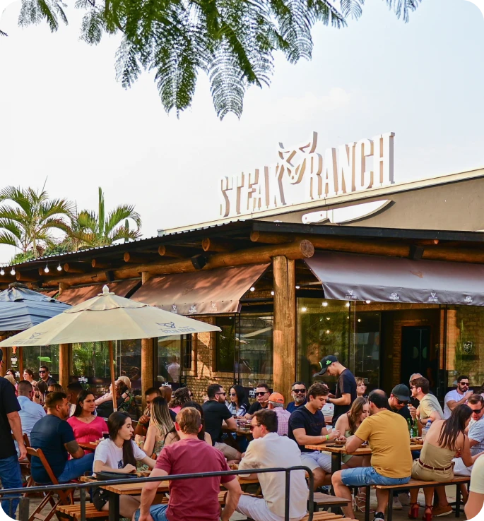 Fachada do restaurante Steak Ranch em Maringá, com clientes sentados na área externa em um dia ensolarado.