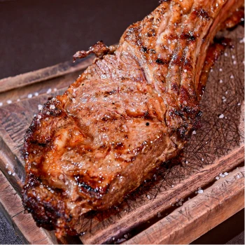 Peça de bife de chorizo grelhada com sal grosso, servida em uma tábua de madeira rústica.